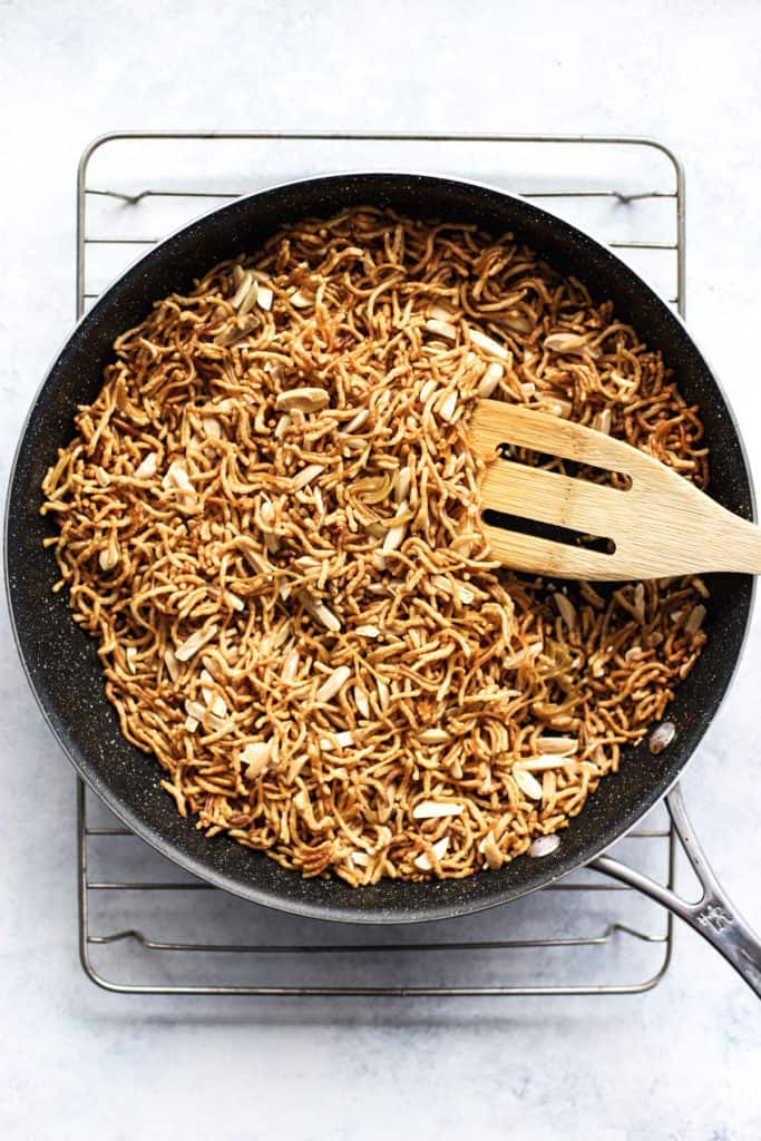 Millet and brown rice ramen noodles, sesame seeds, and slivered almonds in black skillet, after being toasted, on cooling rack