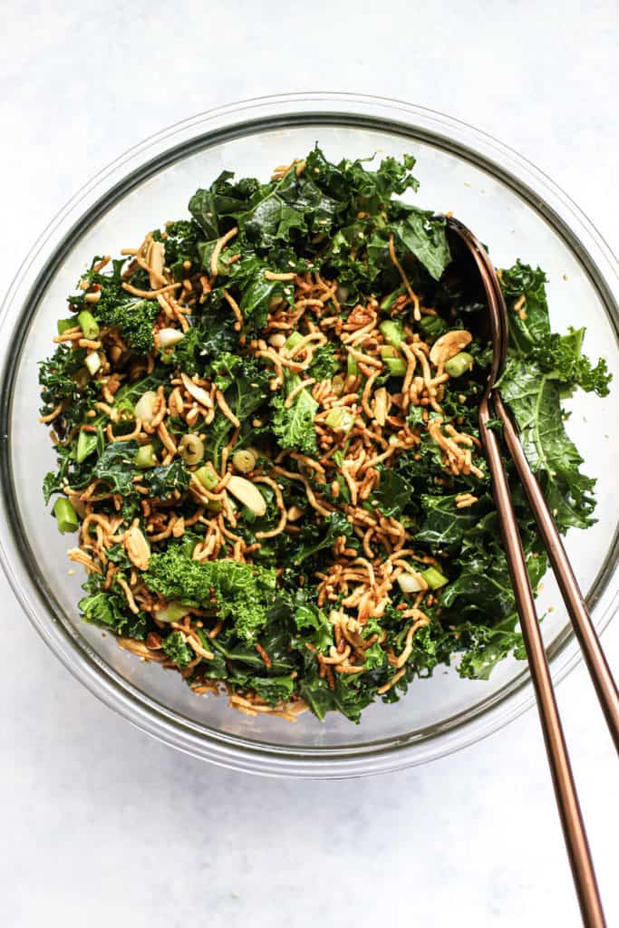 Healthy Asian slaw with ramen in clear glass bowl with two copper serving spoons