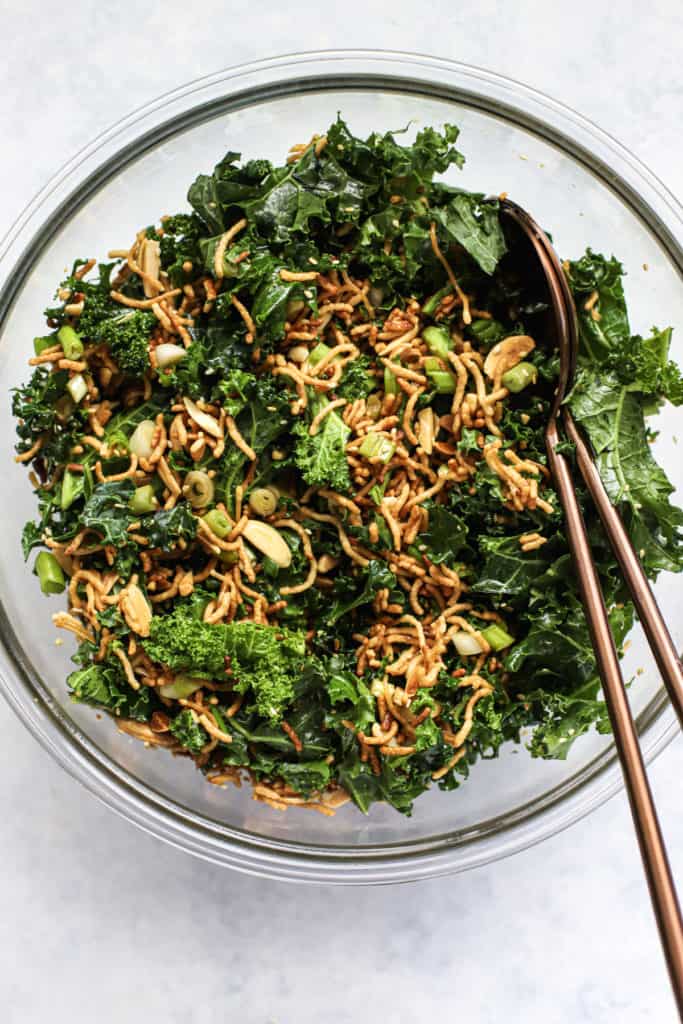 Healthy Asian slaw with ramen in clear glass bowl with two copper serving spoons