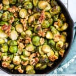 Maple walnut roasted Brussels sprouts in black cast iron skillet, on cooling rack with teal linen and light blue and white background