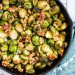 Maple walnut roasted Brussels sprouts in black cast iron skillet, on cooling rack with teal linen and light blue and white background