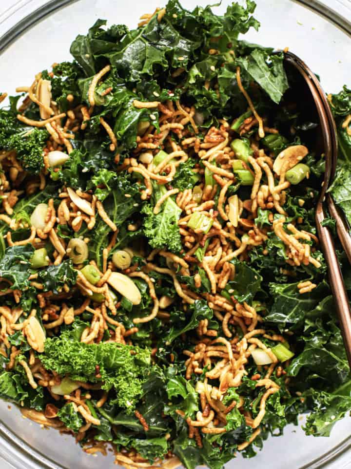 Healthy Asian slaw with ramen in clear glass bowl with two copper serving spoons