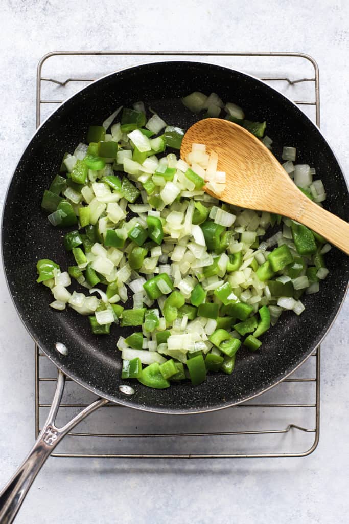Diced green bell pepper and onion being sautéed with bamboo spoon.