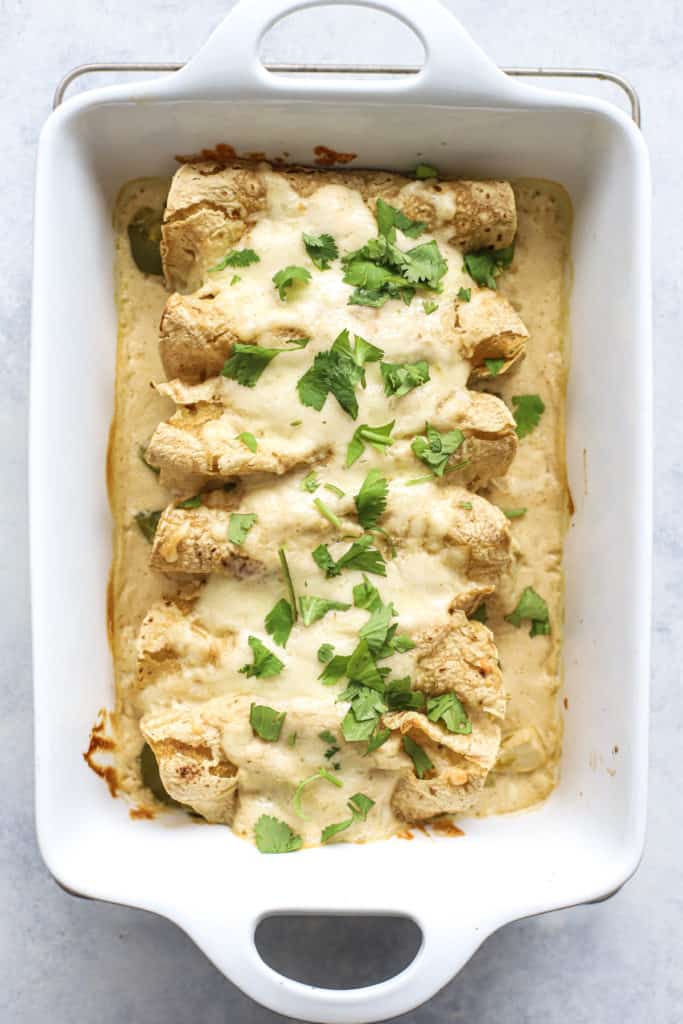 Healthy white chicken enchiladas in rectangular white baking dish, on wire cooling rack, on blue and white surface