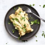 Two healthy white chicken enchiladas on dark gray plate with cilantro and fork