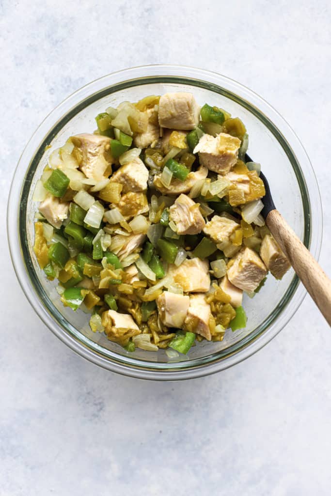 Sautéed pepper and onion, chicken pieces, and green chiles in clear glass bowl on light blue and white surface