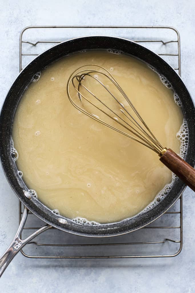 Chicken broth added to white sauce base in dark skillet