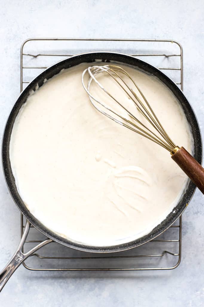 Thick and creamy white enchilada sauce in dark skillet with whisk