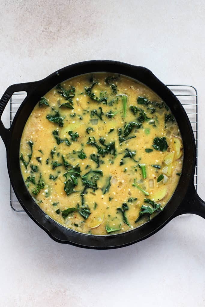 Egg mixture poured into black cast iron skillet with kale, potatoes, and onions.