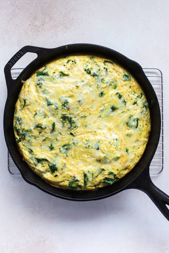 Kale, potato, and onion frittata fresh out of the oven in cast iron skillet, on cooling rack.