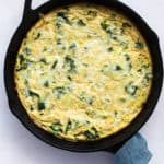 Kale, potato, and onion frittata fresh out of the oven in cast iron skillet, with teal linen wrapped around skillet handle