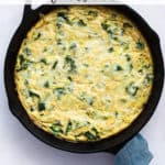 Kale, potato, and onion frittata fresh out of the oven in cast iron skillet, with teal linen wrapped around skillet handle