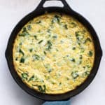Kale, potato, and onion frittata fresh out of the oven in cast iron skillet, with teal linen wrapped around skillet handle