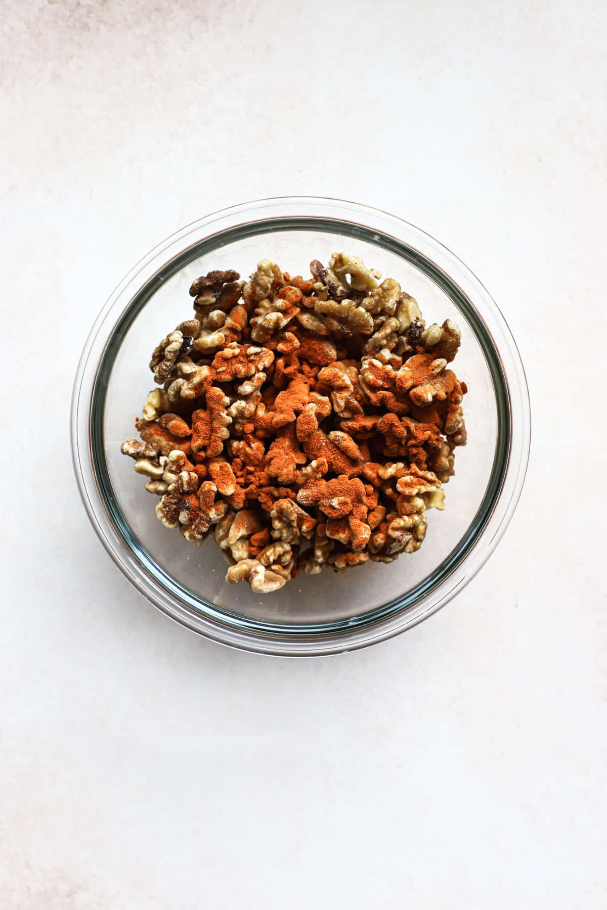 Walnuts, cayenne, and salt tossed together in clear glass bowl.