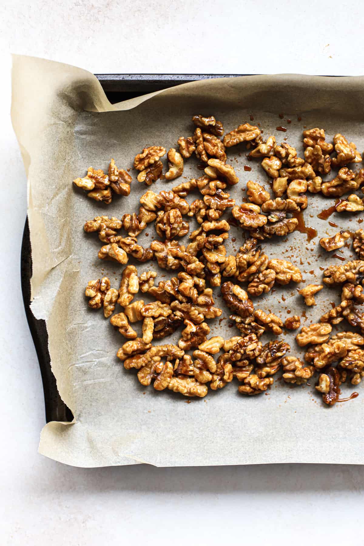 Maple cayenne coated walnuts spread out on parchment-lined baking sheet