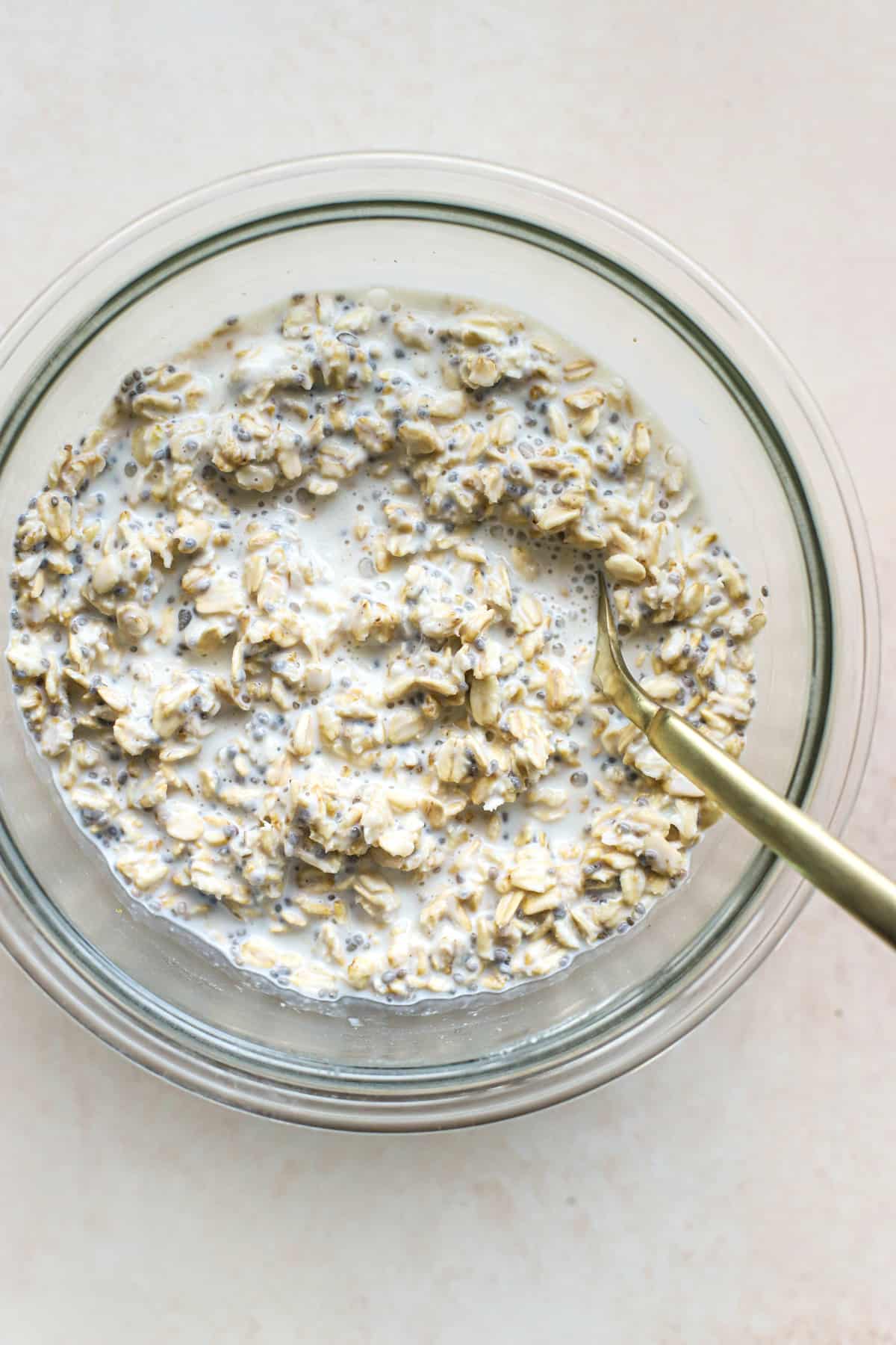 Protein overnight oats in glass bowl with golden spoon, on beige and white surface
