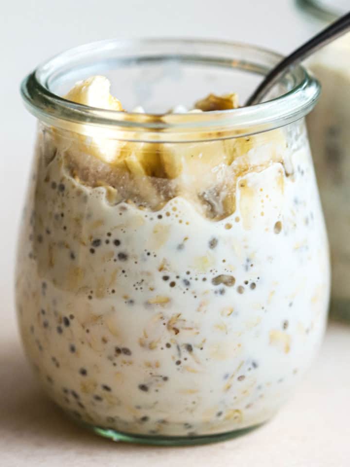 Protein overnight oats in small glass tulip jar with spoon dipped in, and topped with a few banana slices and walnuts