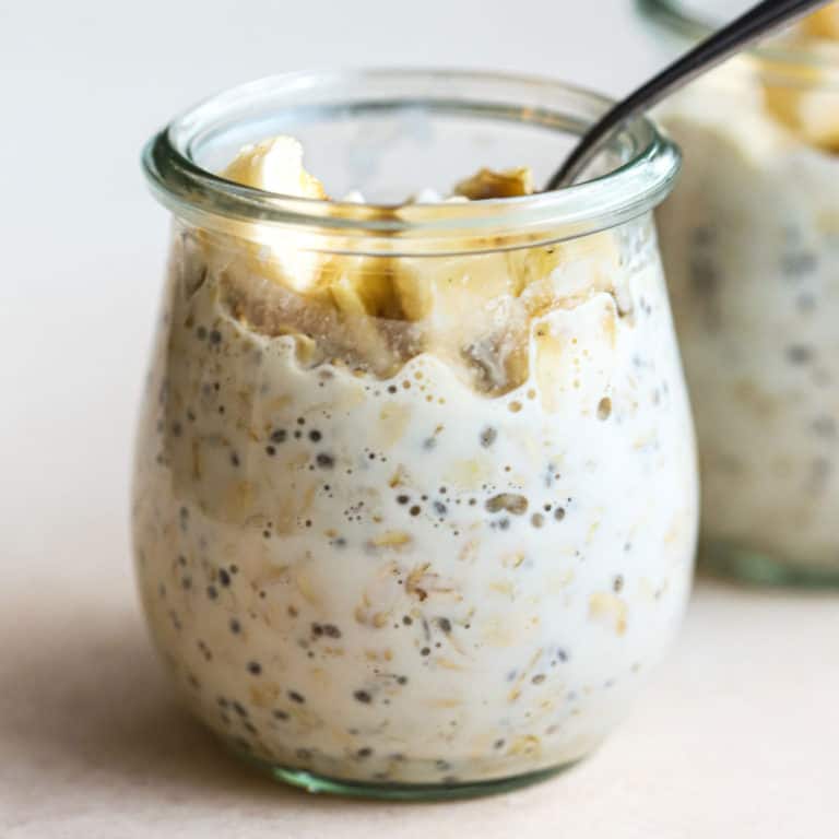 Protein overnight oats in small glass tulip jar with spoon dipped in, and topped with a few banana slices and walnuts