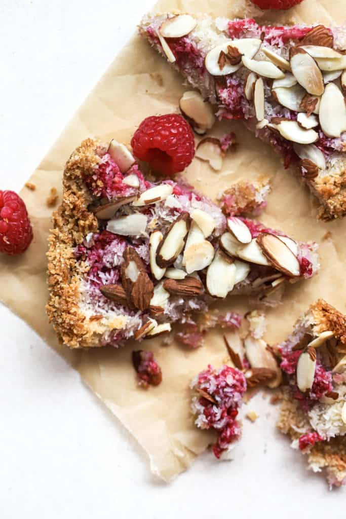 Three pieces of raspberry almond macaroon tart on parchment paper with fork