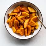 Air fryer butternut squash in beige bowl with gold spoon, on light beige and white surface