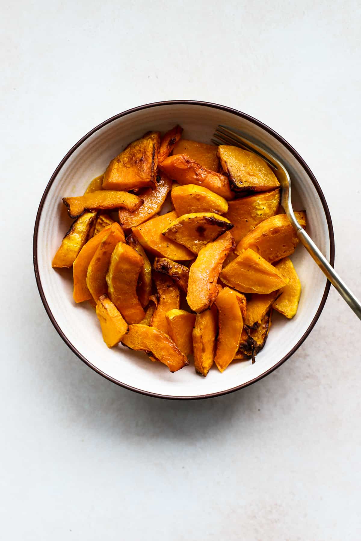 Air fryer butternut squash in beige bowl with gold spoon, on light beige and white surface.