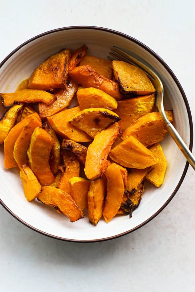 Air fryer butternut squash in beige bowl with gold spoon, on light beige and white surface.