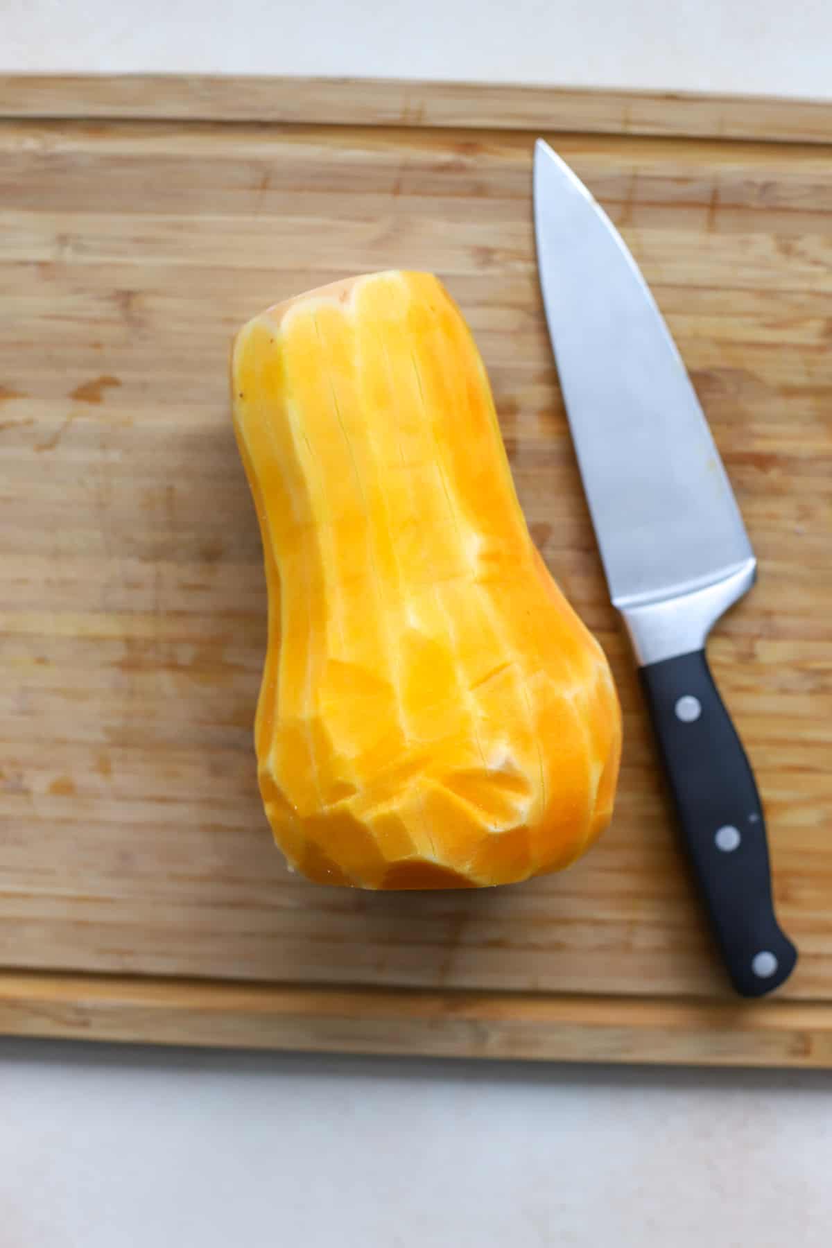 Butternut squash fully peeled, with ends cut off, on cutting board.