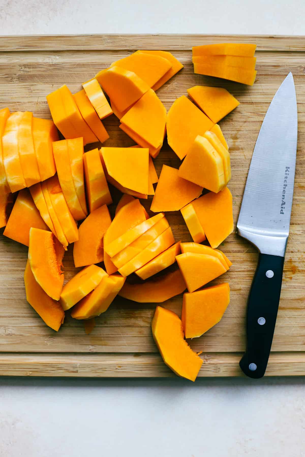 Fully cut up butternut squash pieces on bamboo cutting board next to knife.