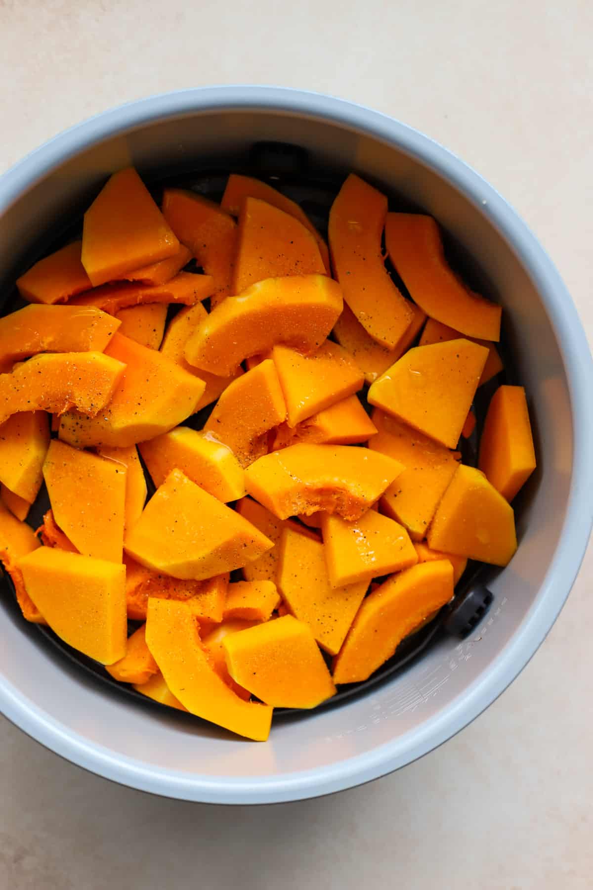 Butternut squash pieces tossed in olive oil, salt, and pepper, in air fryer before being cooked.