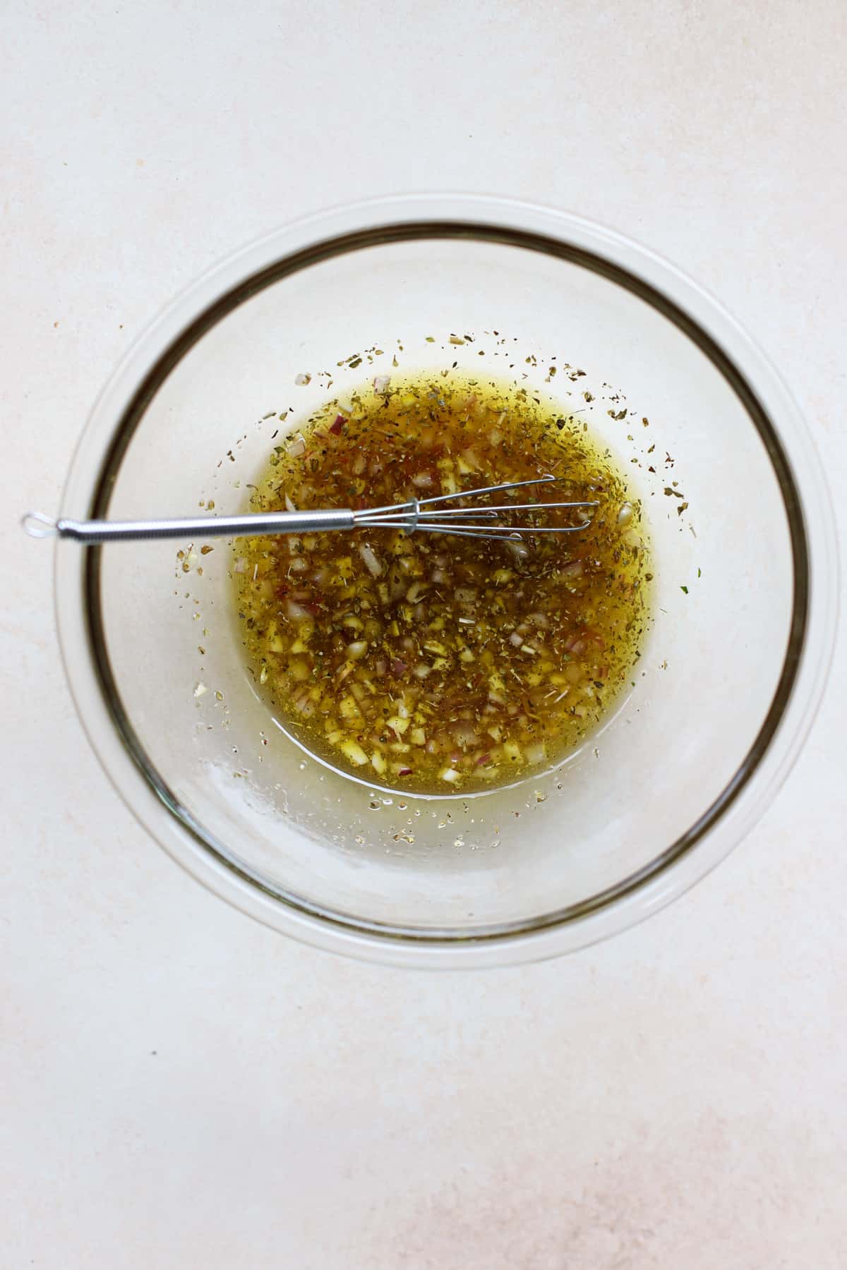 White bean marinade whisked together in clear glass bowl with small whisk on beige and white surface.