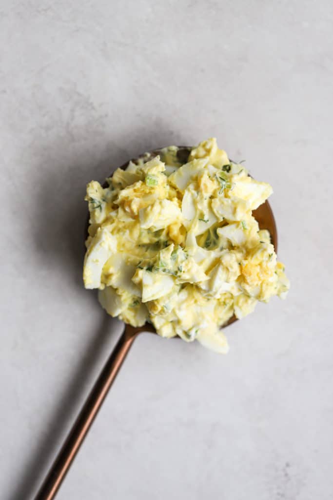 Healthy eggs salad with Greek yogurt dolloped on copper serving spoon, on light gray surface