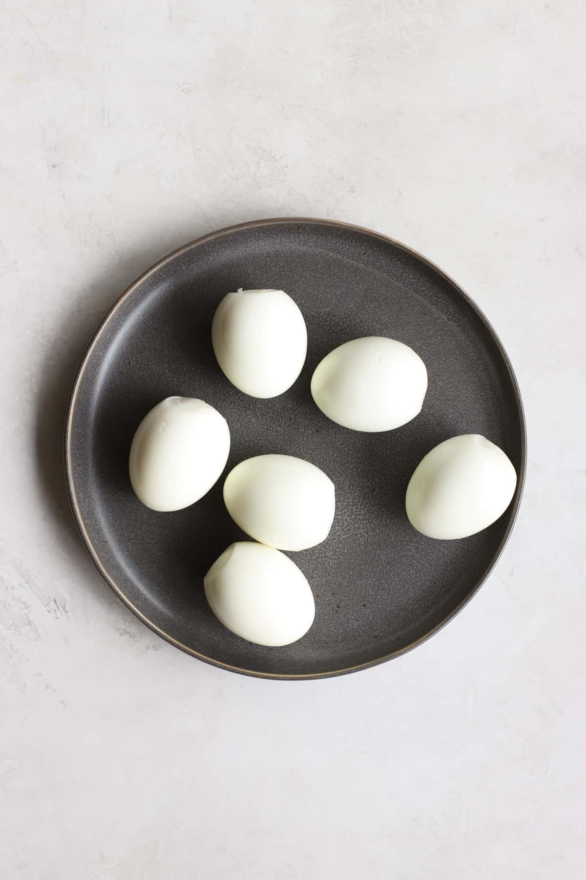 Six peeled hard-boiled eggs on gray plate on light gray surface