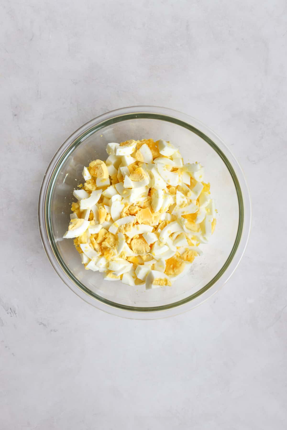 Chopped hard-boiled eggs in clear glass bowl on light gray surface