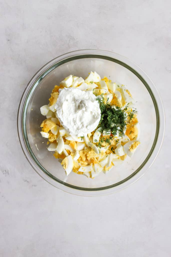 Chopped boiled eggs, Greek yogurt, dill, and mayo in a bowl for egg salad.