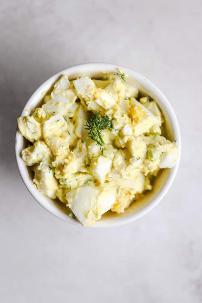Healthy egg salad with Greek yogurt in small white bowl on light gray surface