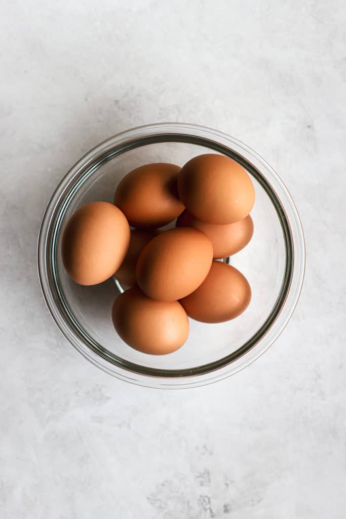 Brown eggs in clear glass bowl on gray and white surface