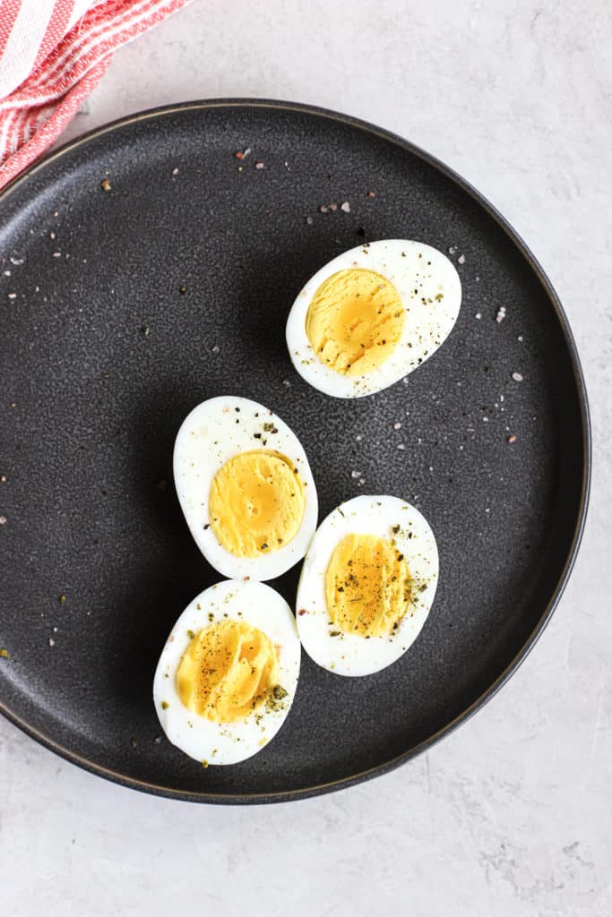 Two Ninja Foodi hard-boiled eggs sliced in half on gray plate, with pink and white linen, on white and light gray surface