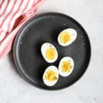 Two Ninja Foodi hard-boiled eggs sliced in half on gray plate, with pink and white linen, on white and light gray surface