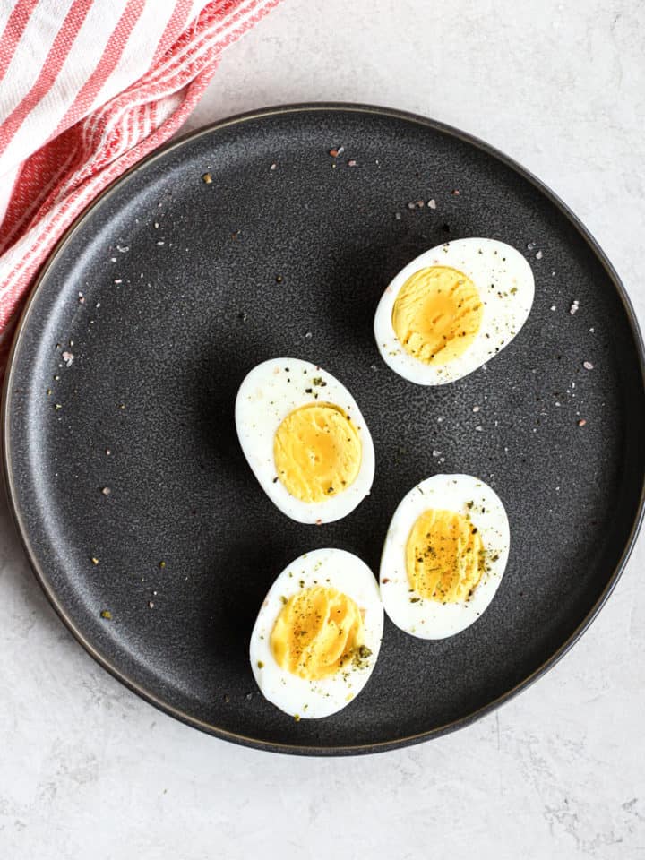 Two Ninja Foodi hard-boiled eggs sliced in half on gray plate, with pink and white linen, on white and light gray surface