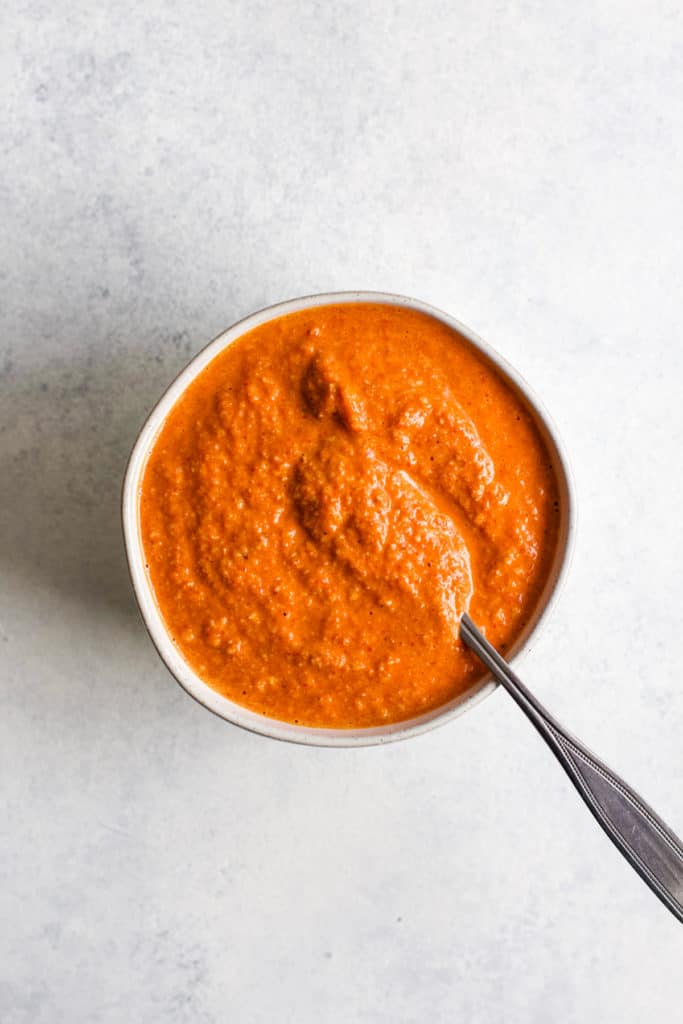 Romesco sauce in small white ball with spoon, on light blue and white surface