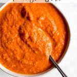 Romesco sauce in small white bowl with spoon, on light blue and white surface