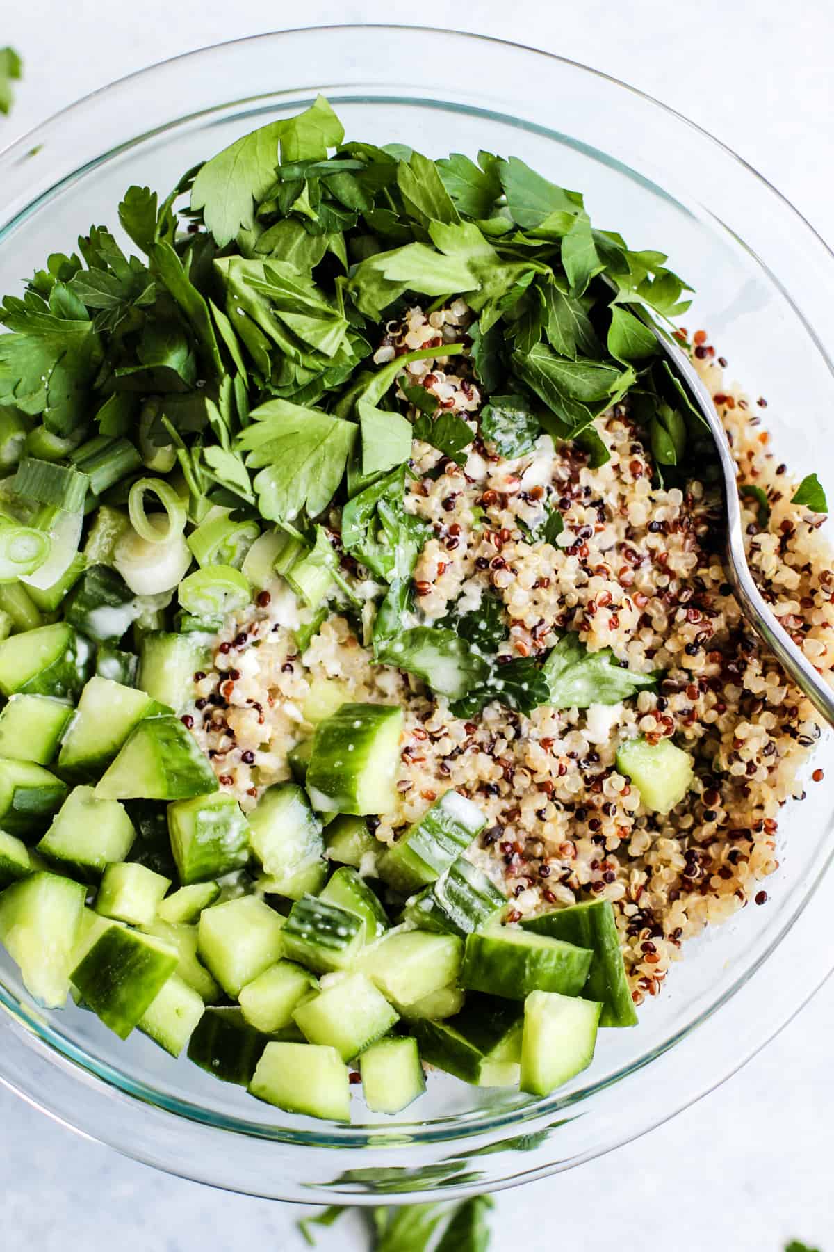 Quinoa, cucumbers, parsley, and green onions, with lemon ginger dressing, in clear glass bowl with spoon.