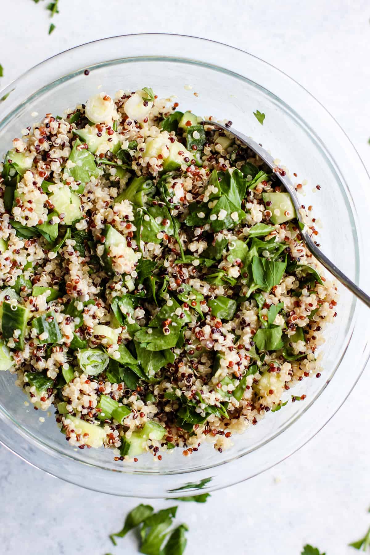 Simple detox quinoa salad tossed together in clear glass bowl with spoon.