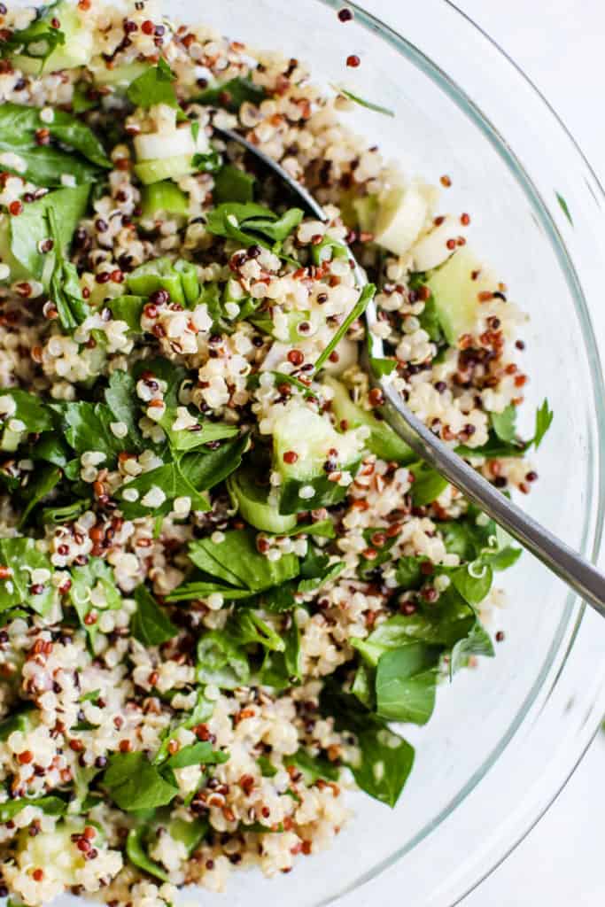 Simple detox quinoa salad in clear glass bowl with spoon.