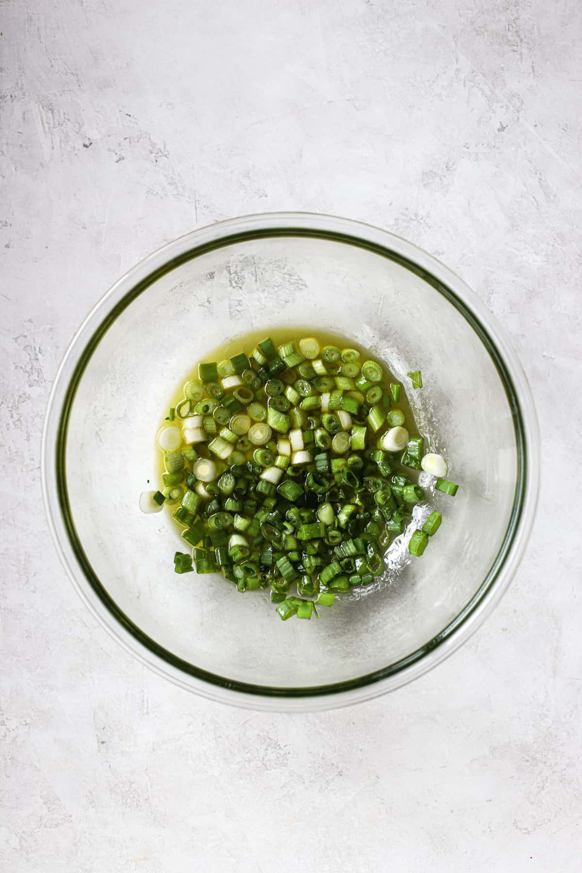 Green onions macerating in coleslaw vinaigrette in clear glass bowl on light gray surface