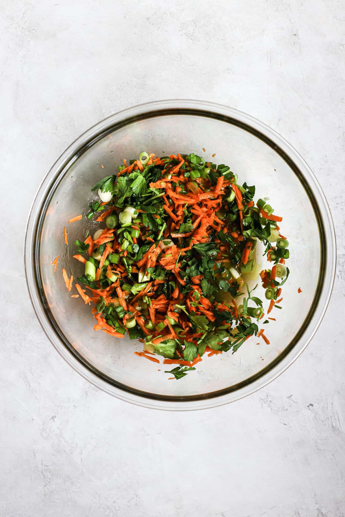 Green onions, carrots, and parsley in coleslaw vinaigrette, in clear glass bowl