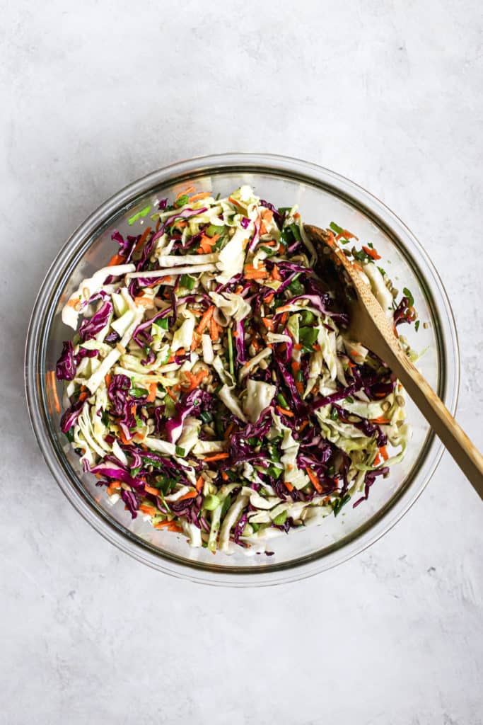 Favorite healthy coleslaw in clear glass bowl with wooden spoon, on light gray surface