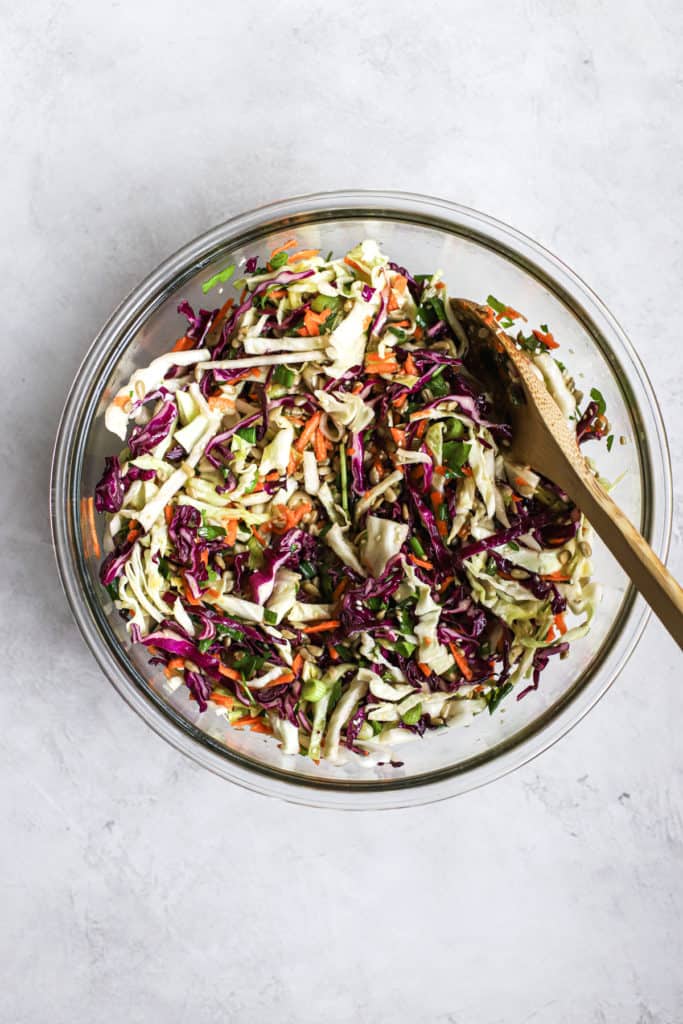 Favorite healthy coleslaw in clear glass bowl with wooden spoon, on light gray surface