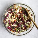 Favorite healthy coleslaw in clear glass bowl with wooden spoon, on light gray surface