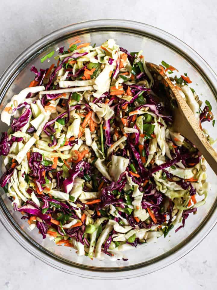 Favorite healthy coleslaw in clear glass bowl with wooden spoon, on light gray surface
